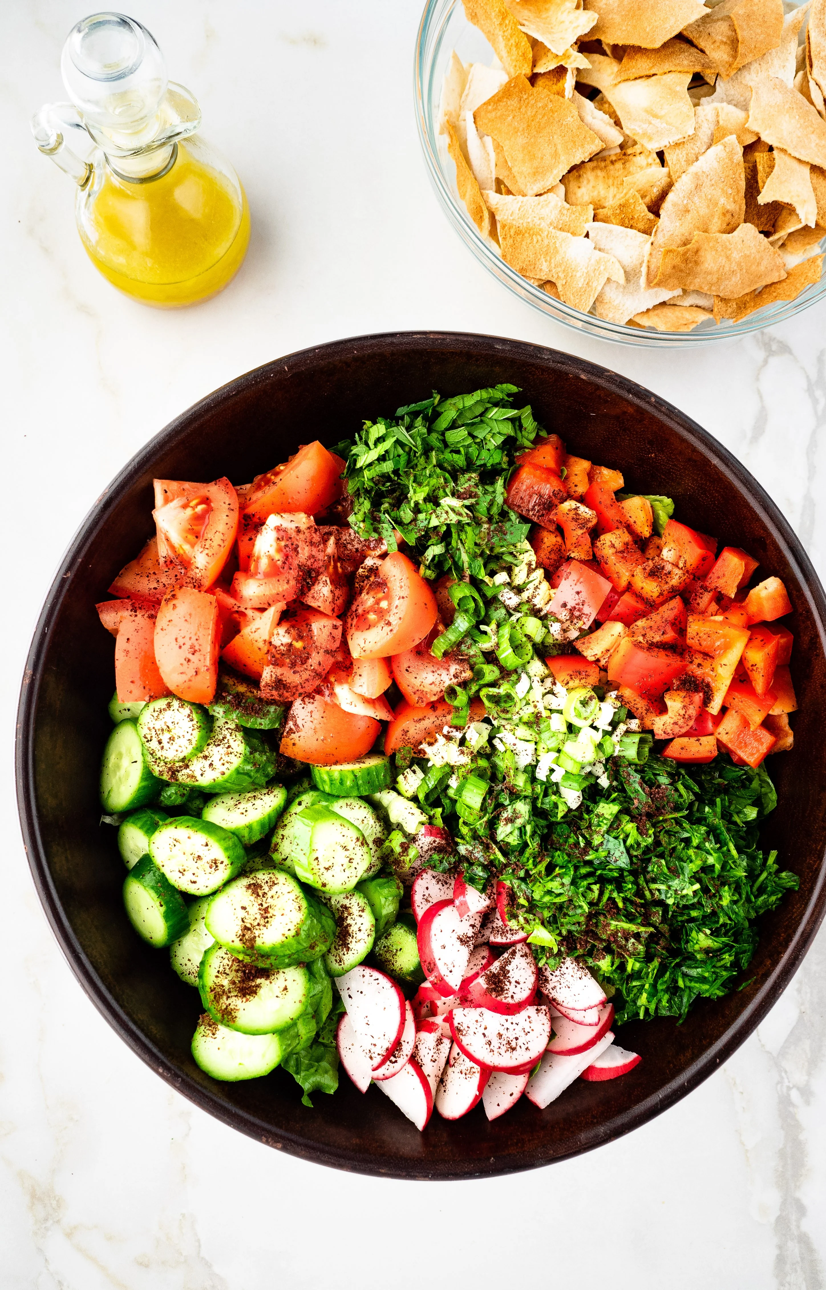 Large bowl of salad with side bowl of toasted pita chips and bottle of salad dressing.