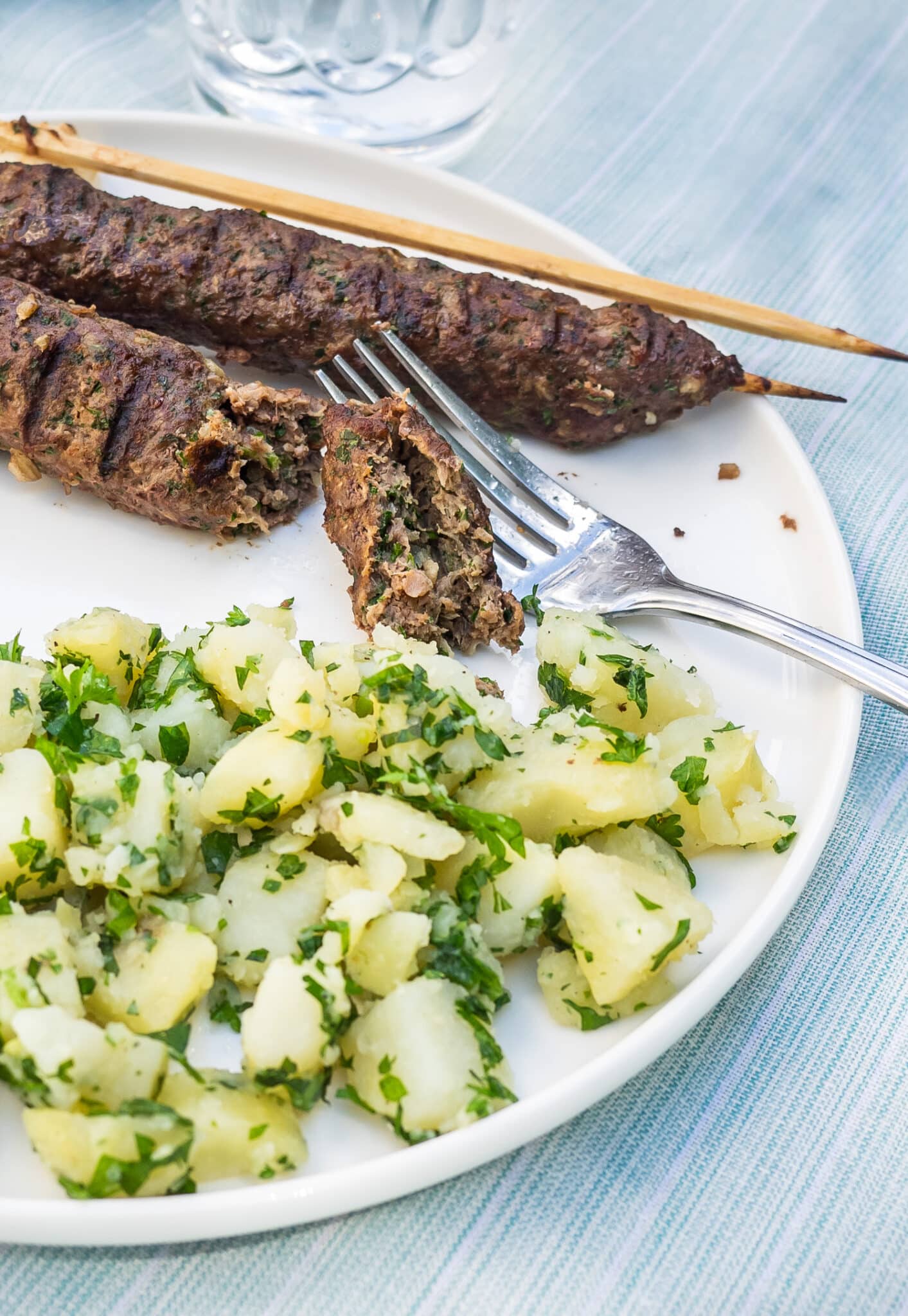 Plate of grilled beef kebabs served with potato salad.