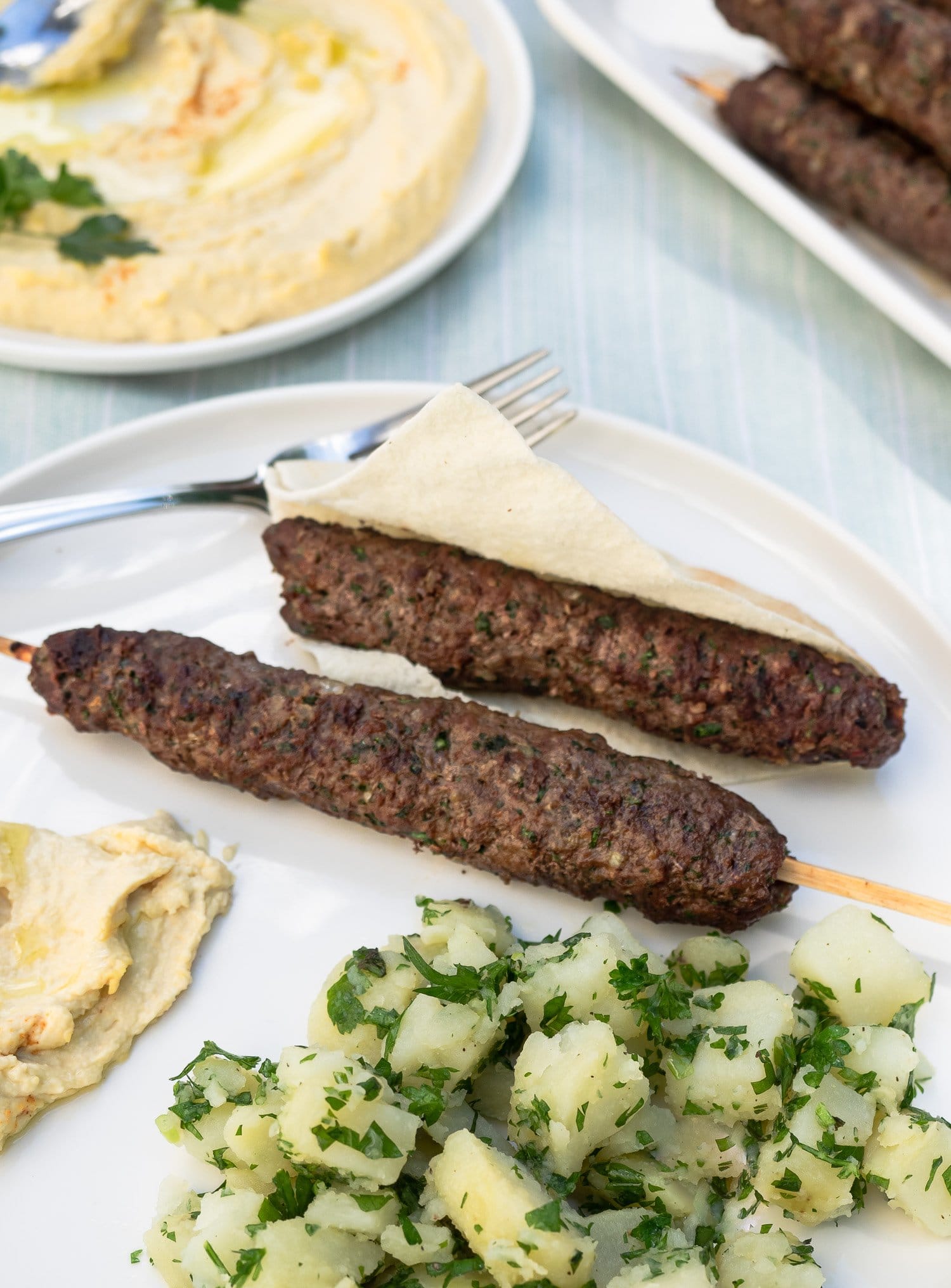 Plate of grilled Kafta served with hummus and Lebanese potato salad.