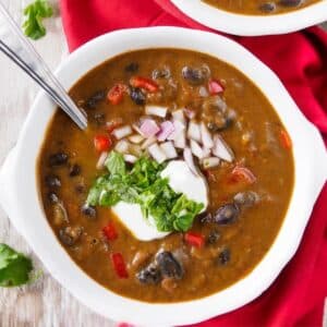 Bowl of black bean soup topped with sour cream, cilantro and chopped red onion.