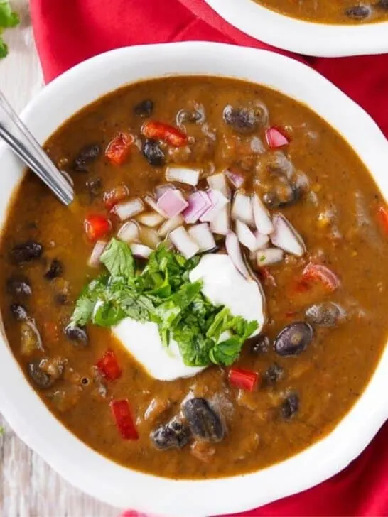 Bowl of black bean soup topped with sour cream, cilantro and chopped red onion.