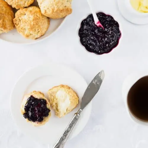 Irish scone topped with butter and berry jam on small dish.