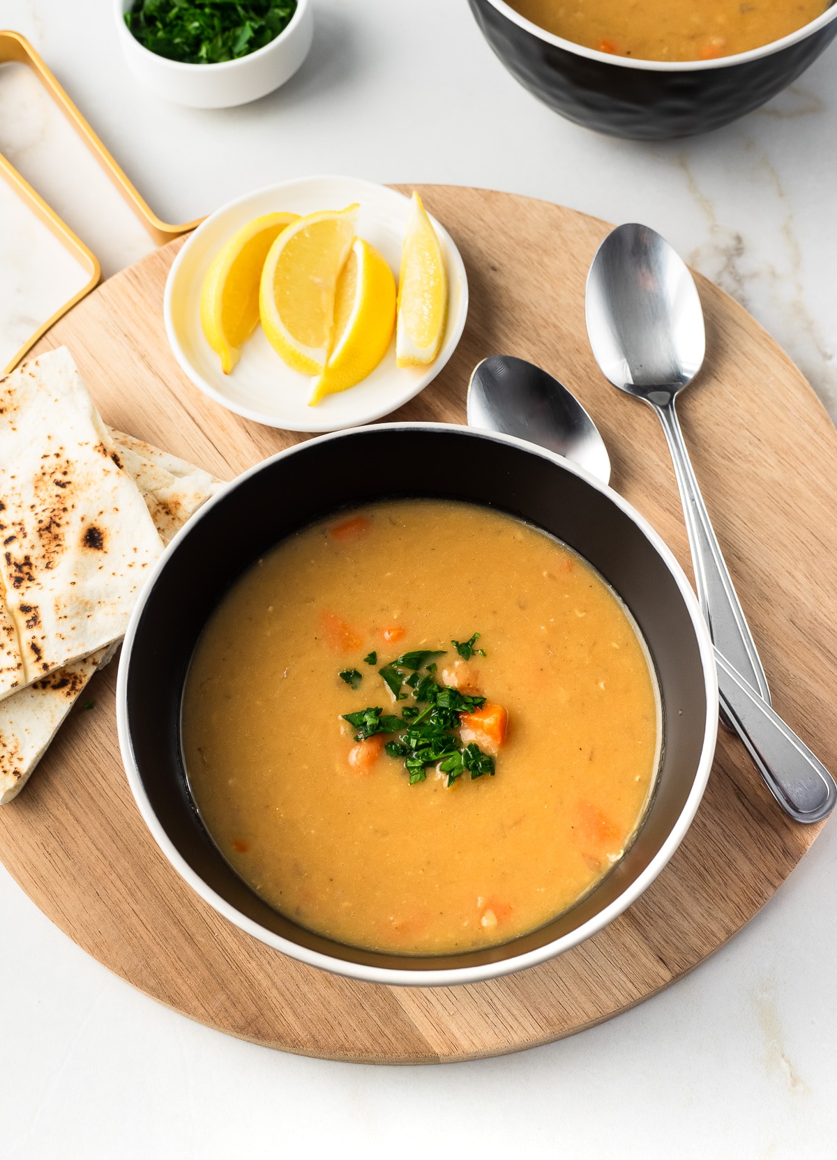 Bowl of red lentil soup served with pita bread and lemon wedges. 