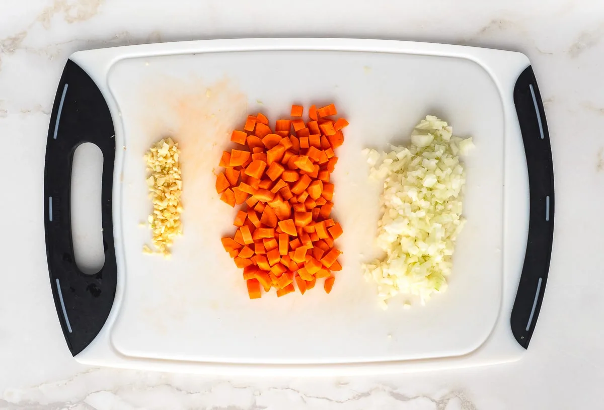 Chopped garlic cloves, carrots and onion on cutting board.