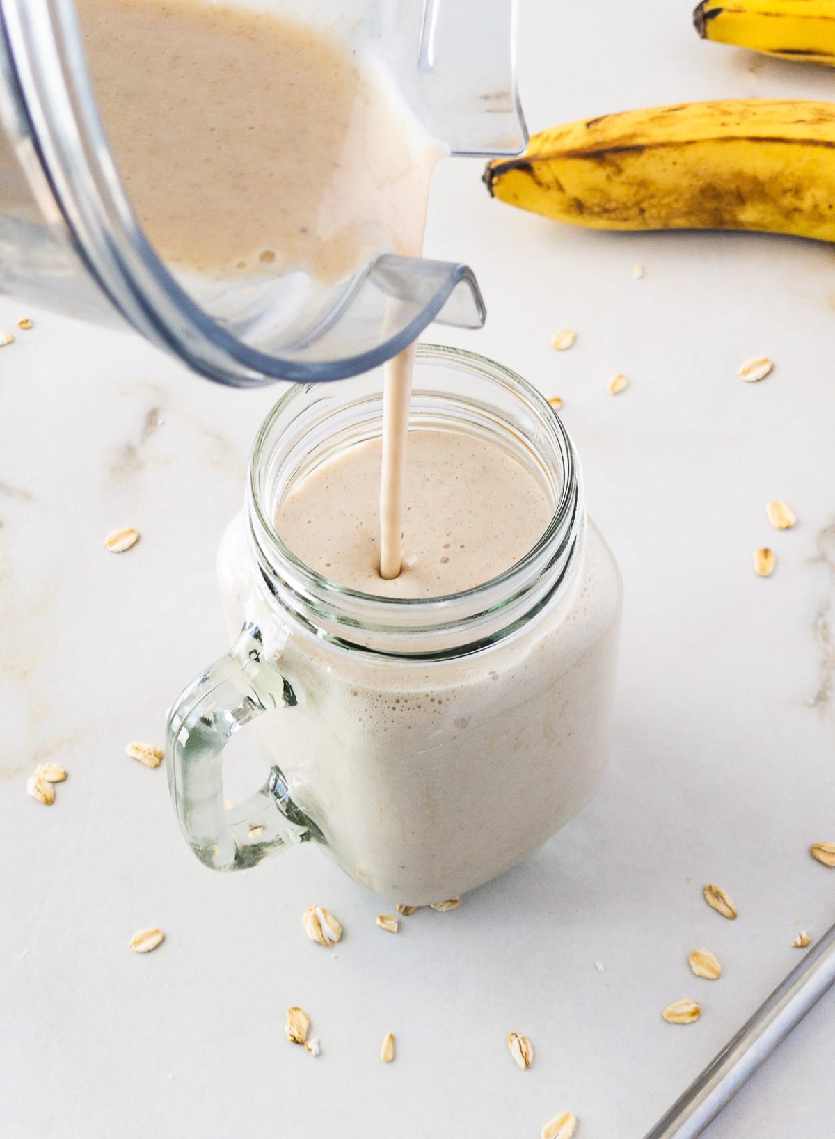 Banana oat smoothie being poured from blender jar into mason jar.