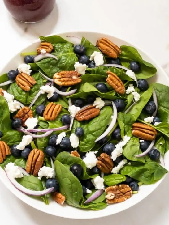 Bowl of blueberry spinach salad topped with pecans, goat cheese and red onion.