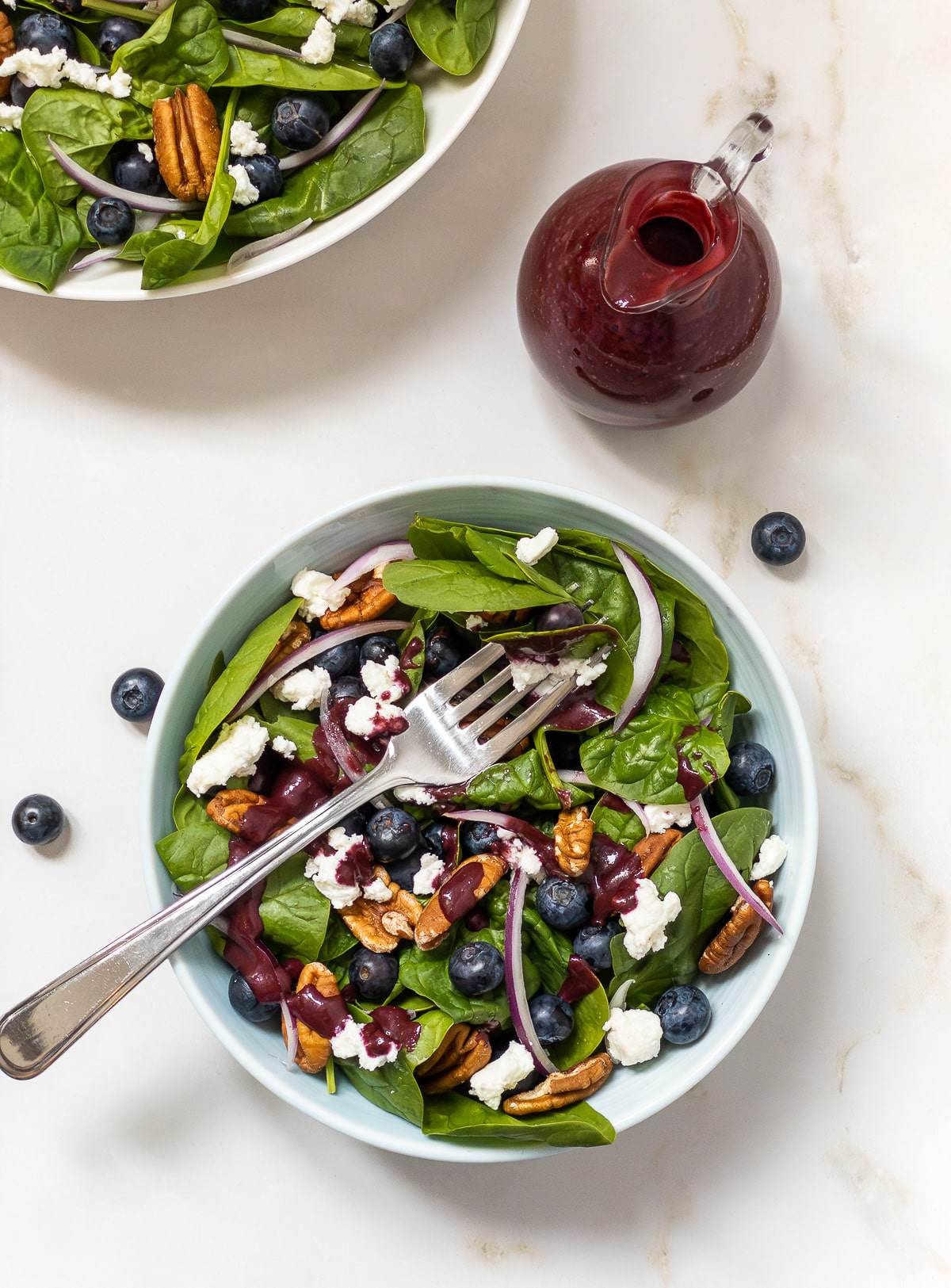 Top view of a small bowl of blueberry spinach salad topped with blueberry balsamic vinaigrette.