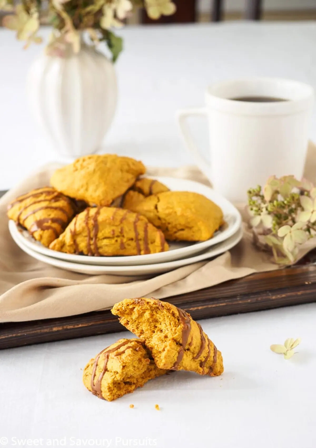 Pumpkin scone broken in half in front of a plate of pumpkin scones.