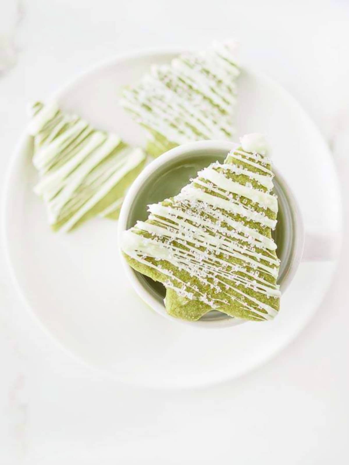 Matcha sugar cookies on dish with one cookie on top of mug.