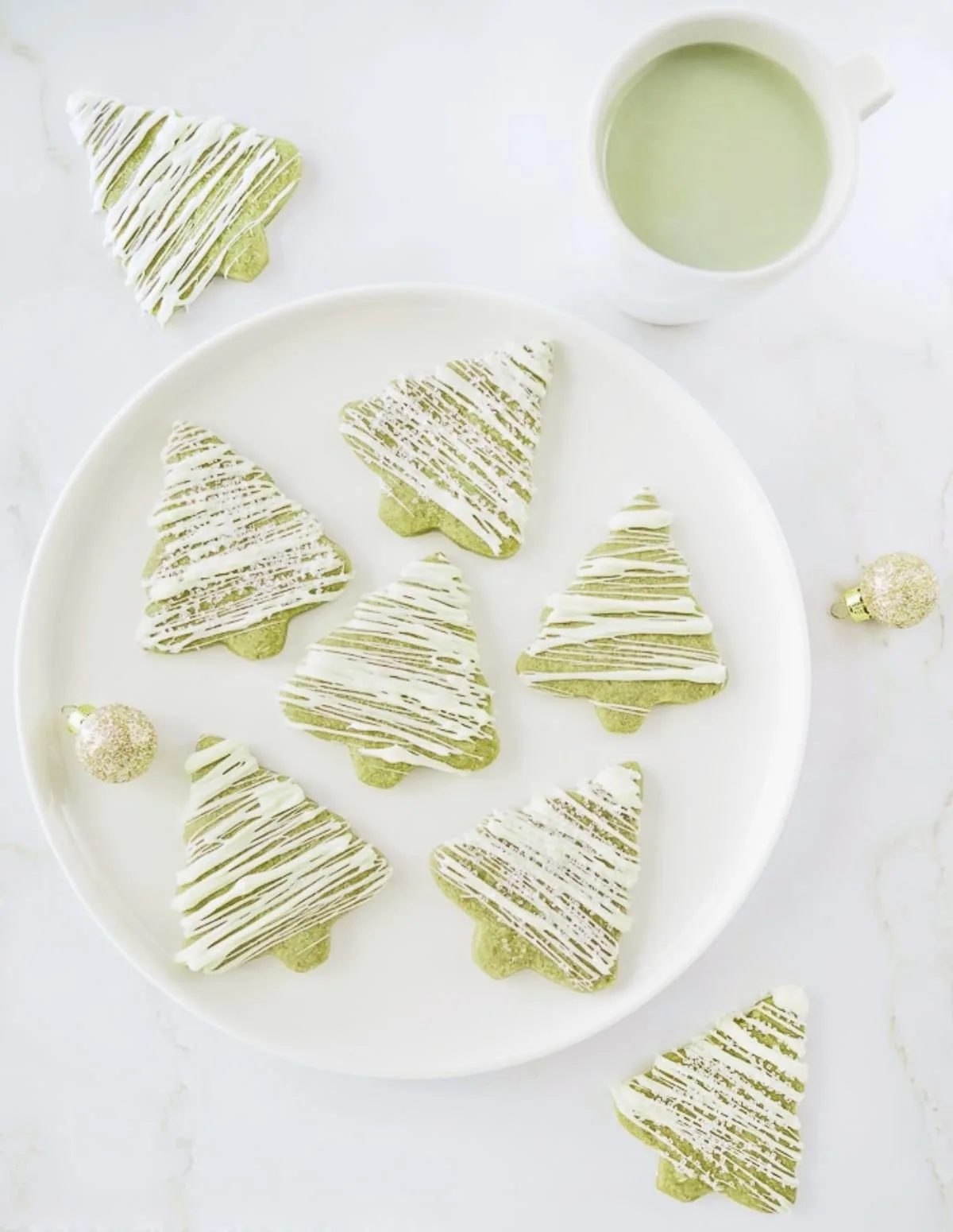 Matcha green tea sugar cookies on white dish with mug of matcha latte.