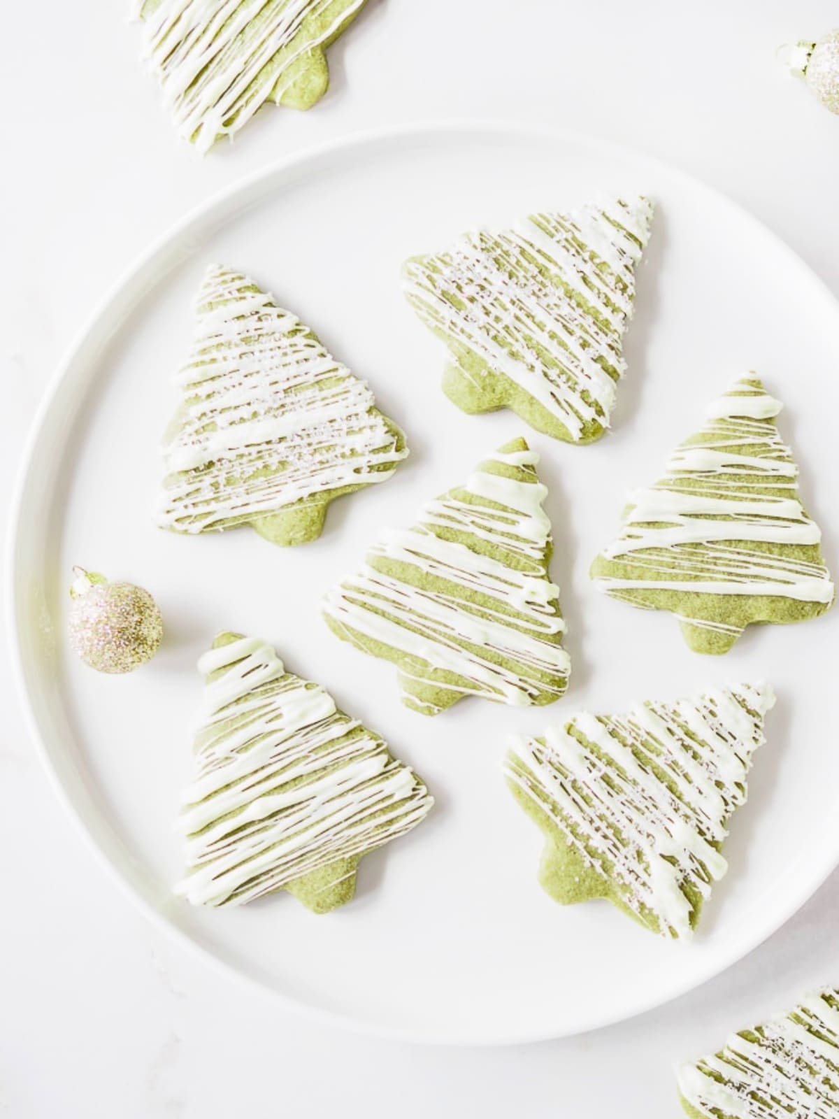 Matcha sugar cookies drizzled with white chocolate icing on white dish.