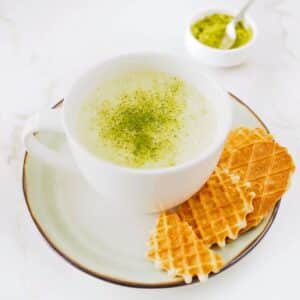 Matcha latte with cookie served on side.