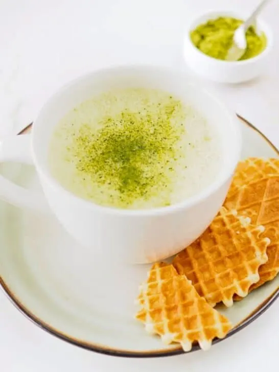 Matcha latte with cookie served on side.