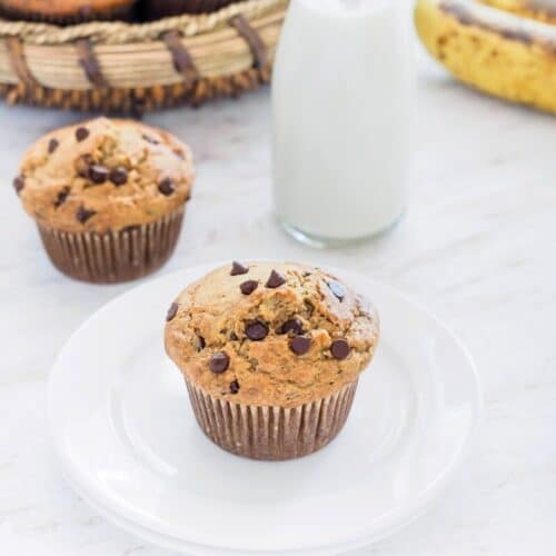 Banana oatmeal chocolate chip muffin on dish served with small bottle of milk.