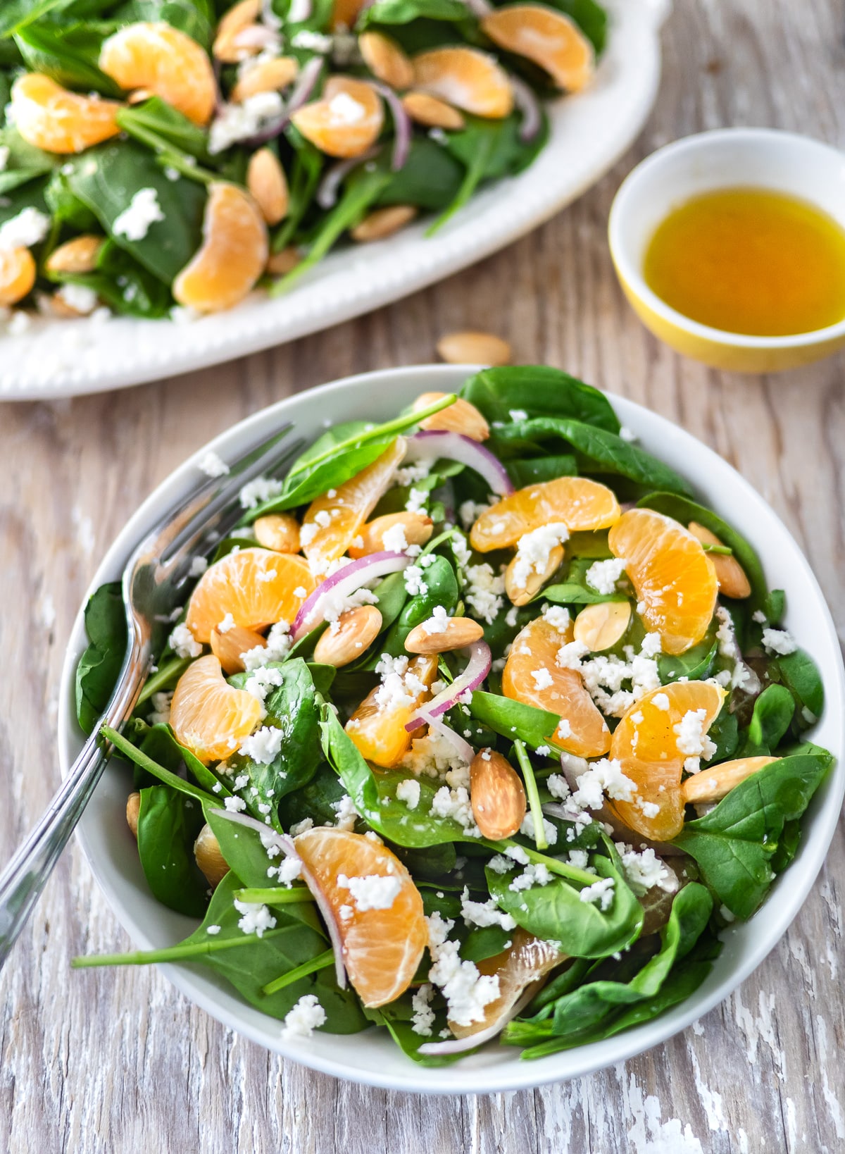 Bowl of spinach salad topped with clementines, almonds and goat cheese.