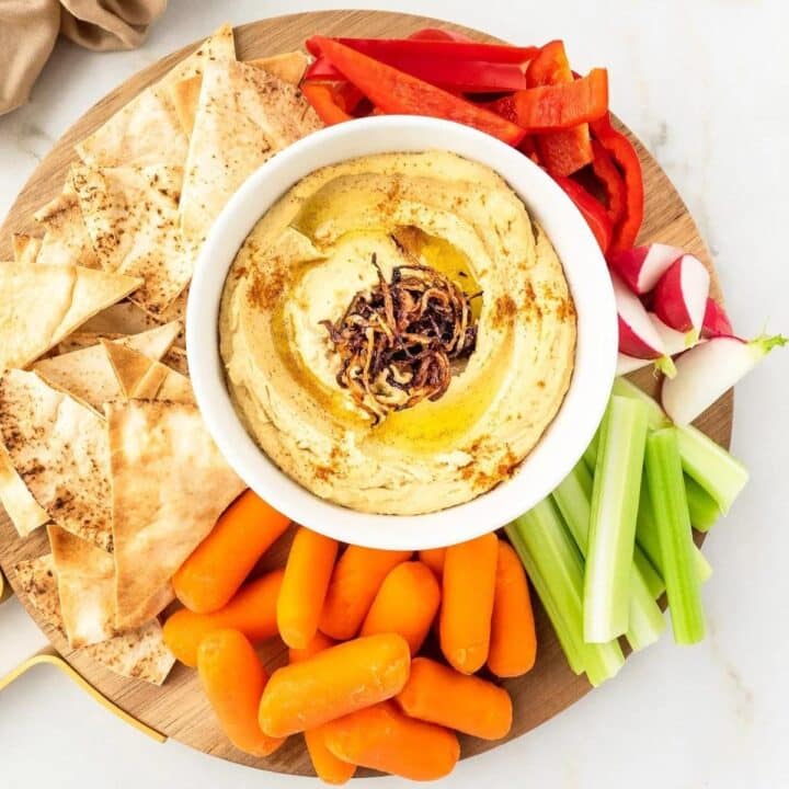 Bowl of caramelized onion hummus served with vegetables and pita.