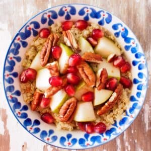 Bowl of quinoa topped with diced pears, pomegranate seeds and pecans.