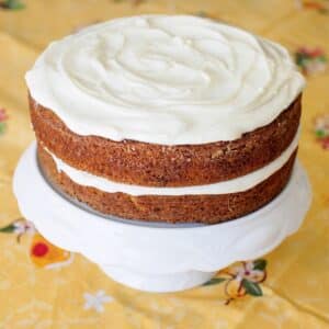 Carrot cake with cream cheese frosting on cake stand.