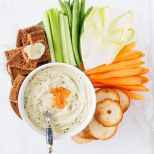 Platter with bowl of smoked salmon dip surrounded with veggies and crackers.