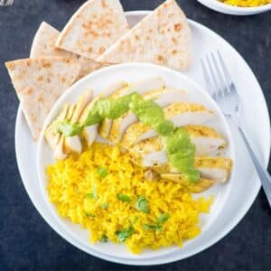 Plate of Indian style yogurt marinated chicken breasts served with rice and cilantro sauce.