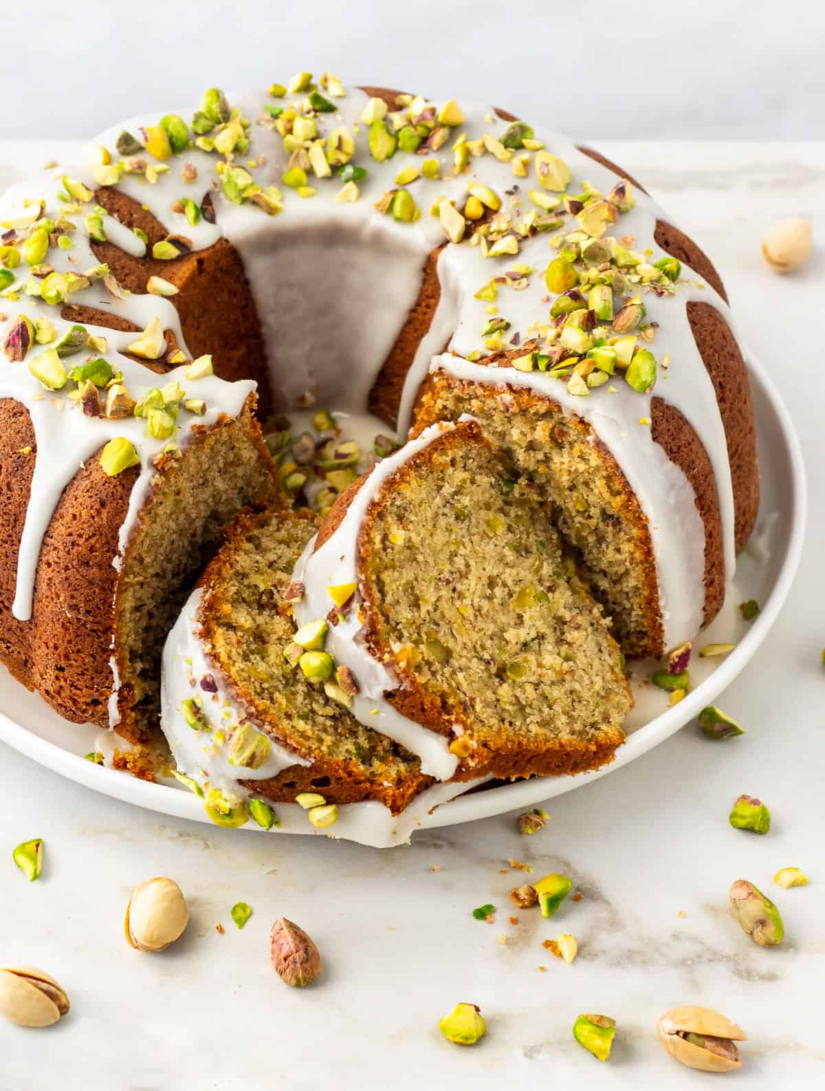 Close-up of a pistachio bundt cake drizzled with glaze on platter.