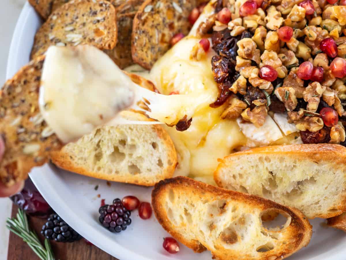 Close-up of a slice of baguette with melty stretchy Brie on it.